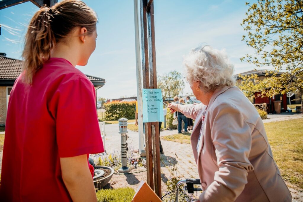 Vårdpersonal går med äldre dam på tipspromenad