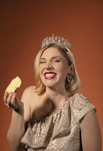 Agnes Forstenberg ler stort med tiara i håret och ostsmörgås i handen. Foto.