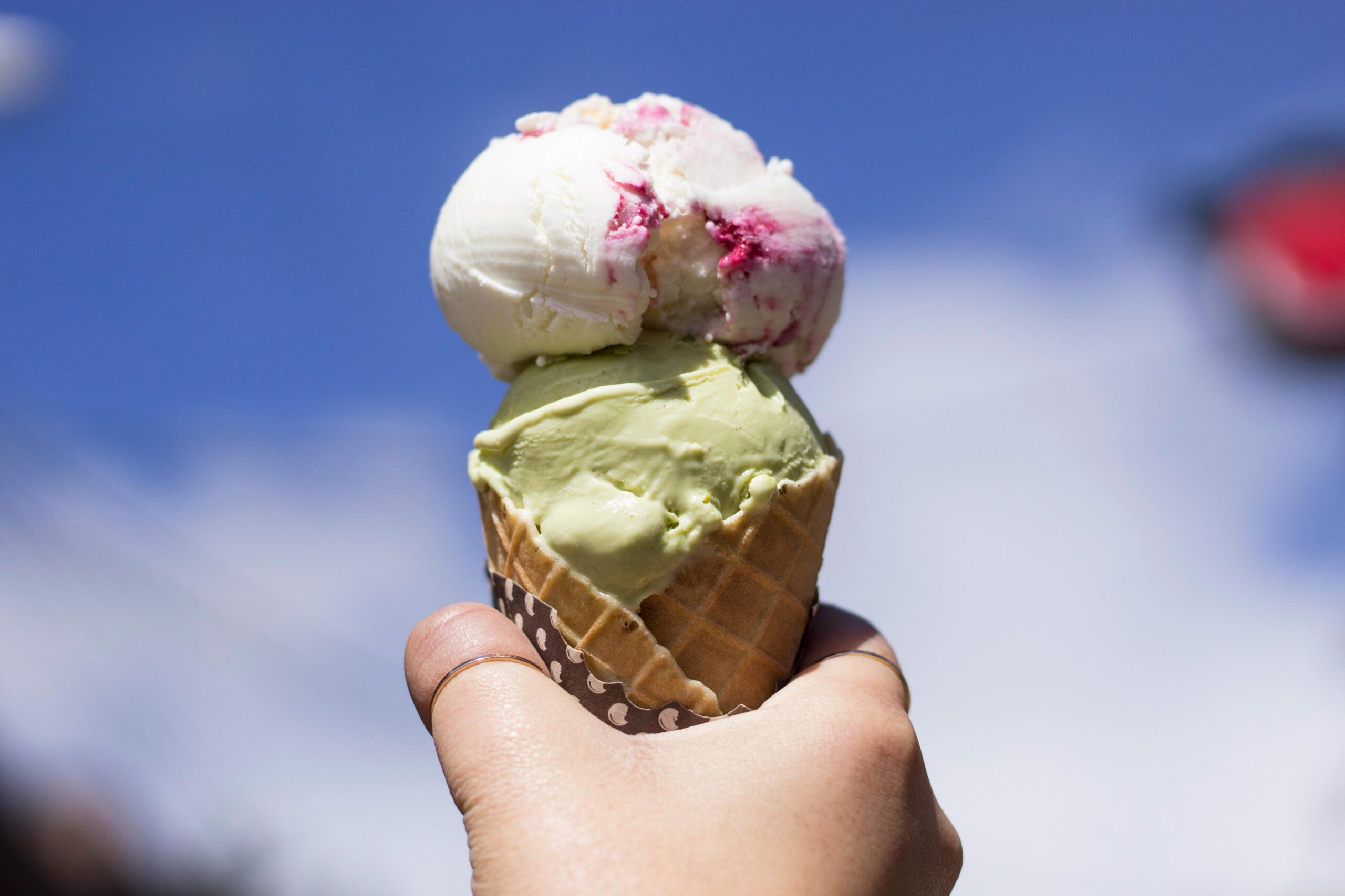 En hand håller i en glasstrut med en rosa och en grön glasskula
