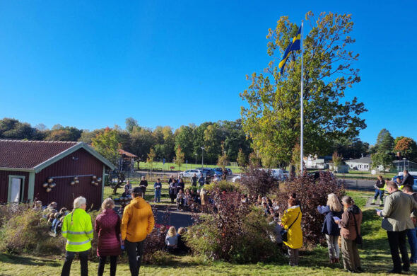 Grupper med personer står samlade på en skolgård. Det är invigning av skolans nya lokaler och skolgården är fylld med barn, lärare och andra vuxna som deltar i festligheterna.